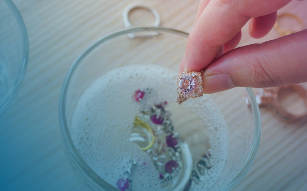 Person holding a luxury ring while cleaning it, with other fine jewelry sitting in a cleansing solution.